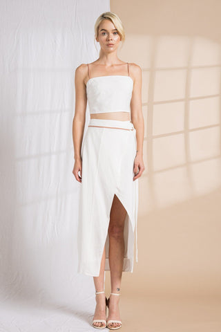 Model wearing a two-piece, wrap skirt and crop top set. She is standing in front of a backdrop that is half tan and half white. She is facing forward to show the details on the belt of the skirt.