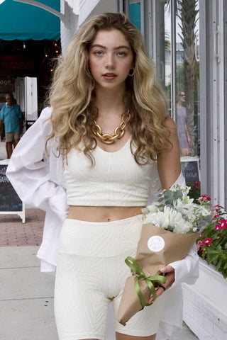 Model wearing zebra-texture, two piece, athleisure set. She is standing on a sidewalk, holding flowers, and looking into the camera. 
