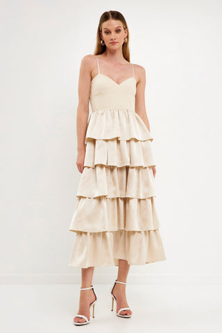Model wearing champagne color dress with tiered ruffles on the skirt. The top is a spaghetti strap, sweetheart neckline bust.Model is standing in front of a white background and the image shows her whole body.