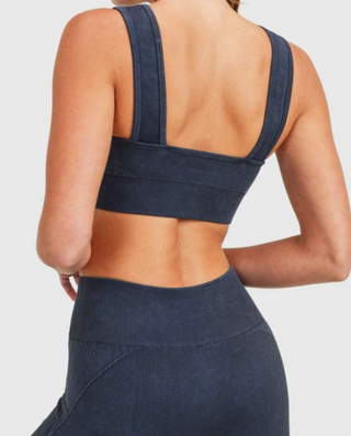 Model wearing black washed, ribbed, sports bra. She is standing in front of a white backdrop and is facing backwards to show the back of the set.