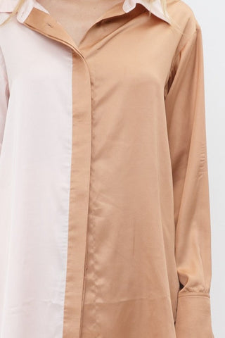 Model is standing in front of white backdrop. She is wearing a satin long sleeve top and satin pant set. The top is a color block satin top with one side peach and one side light pink. The pants are a color block satin pant with one side peach and the other side light pink. The photo is up close of the top only. 