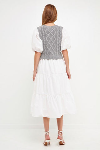 Model wearing white dress with grey cable knit sweater over the dress. Model is standing in front of white backdrop. Photo is taken from the back to show the back of the dress. 
