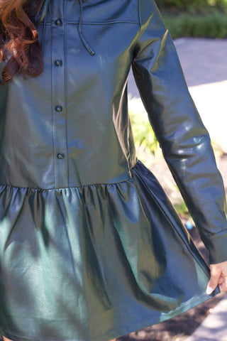 Model is wearing deep green vegan leather dress with drop waist, high collar and long sleeves. Photo is up close to show the detail of the skirt. 