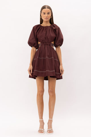 Brown cut out midi dress with white thread detailing, puff sleeves, and a bow enclosure. Model is standing in front of white background.