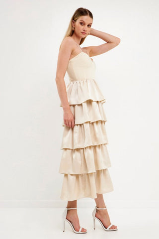 Model wearing champagne color dress with tiered ruffles on the skirt. The top is a spaghetti strap, sweetheart neckline bust.Model is standing in front of a white background and the image shows her whole body.