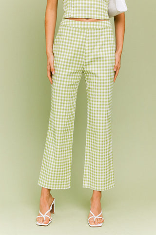Model wearing a green and white gingham matching set. The top is a gingham corset, tube top. The pants are a straight leg, cropped gingham pant.  Model is standing in front of green background. 