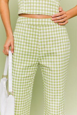 Model wearing a green and white gingham matching set. The top is a gingham corset, tube top. The pants are a straight leg, cropped gingham pant.  Model is standing in front of green background. Close up of front of pant. 
