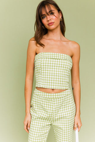 Model wearing a green and white gingham matching set. The top is a gingham corset, tube top. The pants are a straight leg, cropped gingham pant.  Model is standing in front of green background. 