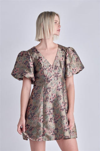 Model is standing in front of white background. She is wearing the jacquard print mini dress in the color olive, burgundy, and light pink. The dress has puff sleeves and a deep v neckline. 