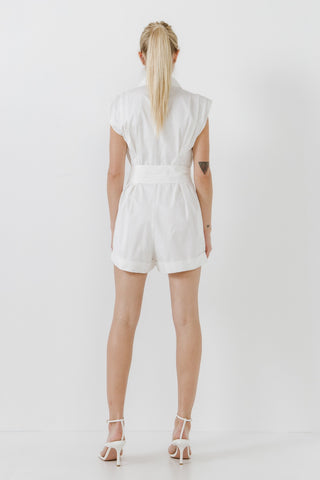 Model wearing white, collared, cotton, belted romper. She is standing in front of a white backdrop. The model is facing backwards to show the back of the romper.