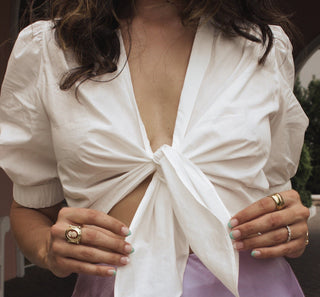 Up close image of the white cropped top that ties in the front. The model is holding both ends of the knot which tied both sides of the blouse together. An up close image.