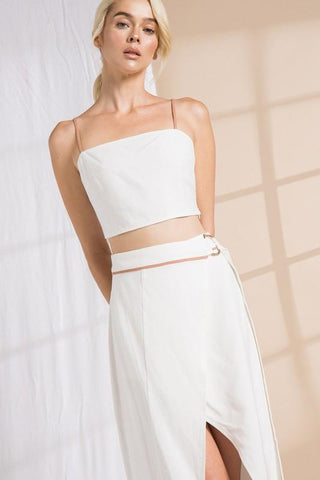 Model wearing a two-piece, wrap skirt and crop top set. She is standing in front of a backdrop that is half tan and half white. She is up close to show the details on the belt of the skirt.